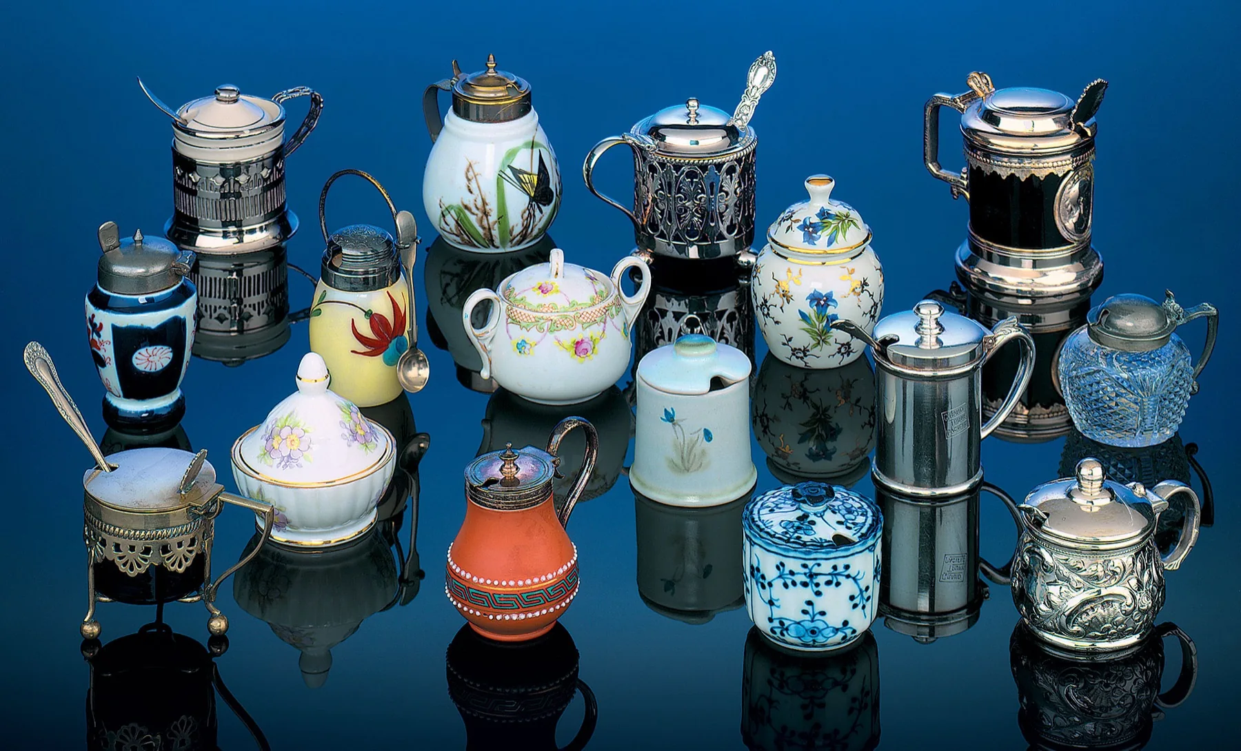 Antique mustard pots in porcelain, silver and stoneware against a deep blue ground
