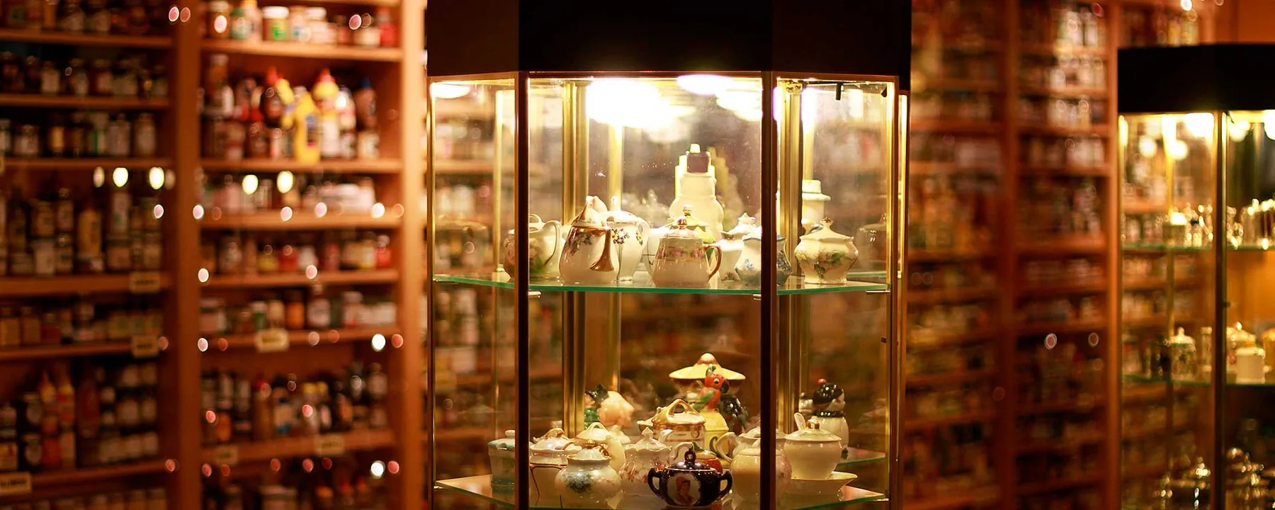 Porcelain mustard pots in a lit case with the museum’s wall of jars behind